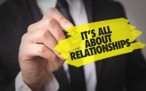 a man in a black suit holds a yellow sign that reads "it's all about relationships"